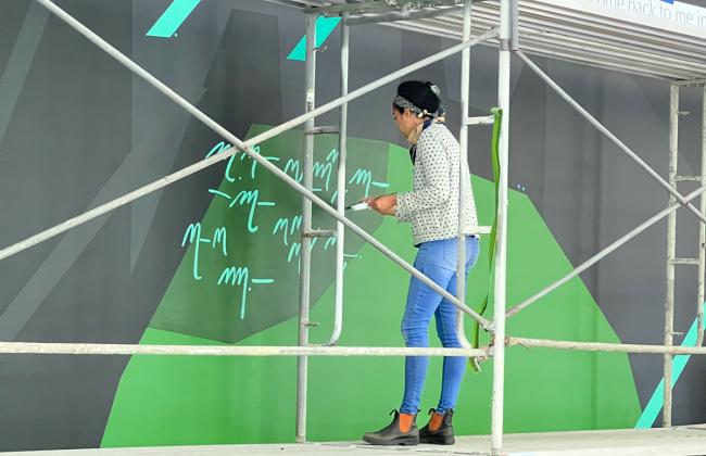 The artist Caroline Kent stands on a scaffold applying detail to her mural.