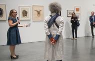 Curator Apsara DiQuinzio holds a microphone while addressing a tour group within a gallery at BAMPFA.