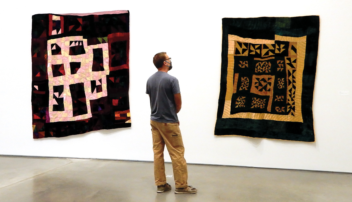 A man looks at two quilts by Rosie Lee Tompkins hung on a white wall in a gallery.
