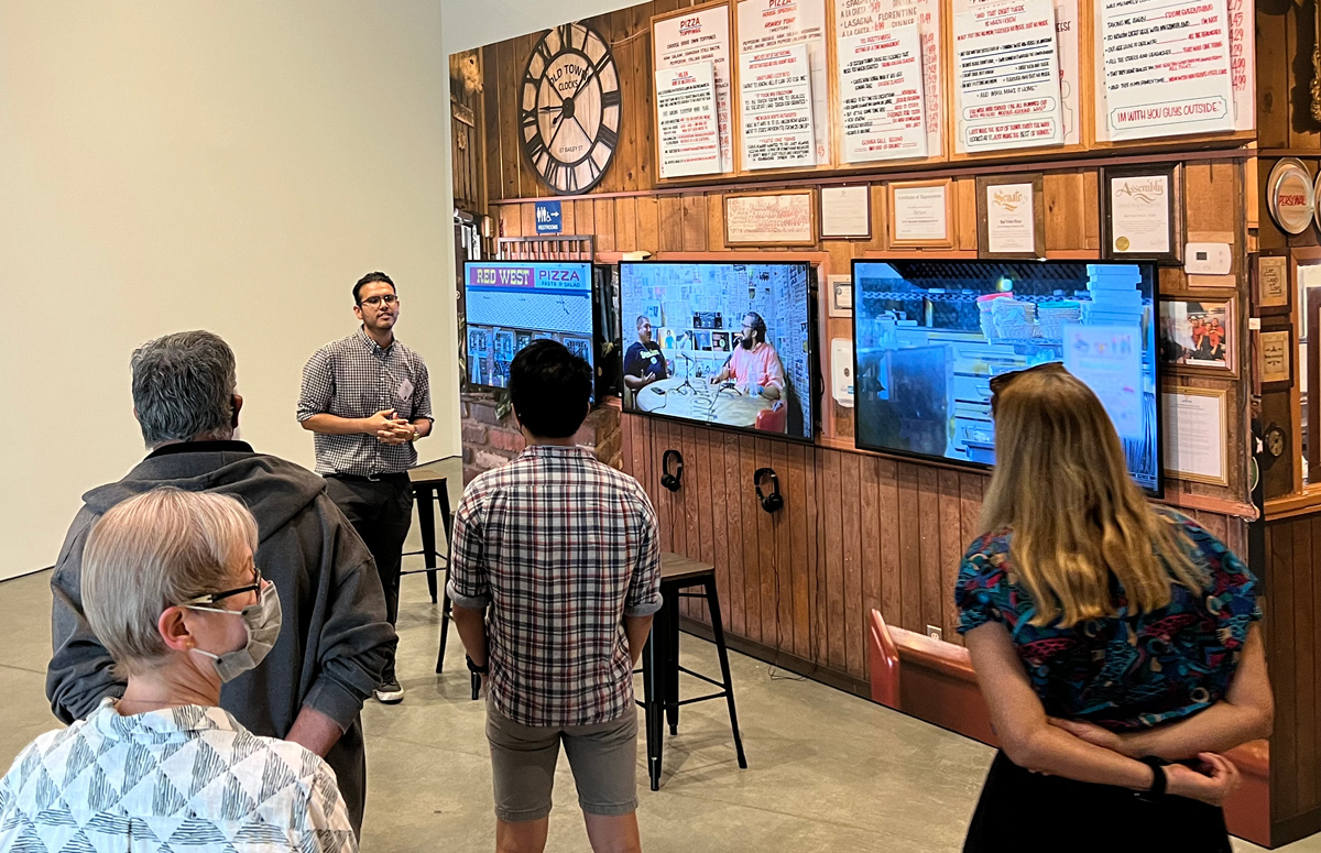 Pictured: Underground Scholars program guide Eli Martinez leads a tour of the exhibition Undoing Time, speaking in front of Mario Ybarra Jr.'s large-scale installation.
